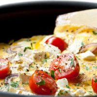 Cooking omelet in a pan, ready to serve.  With Cherry tomatoes, red onion, goat's cheese and parsley.  Shallow DOF.