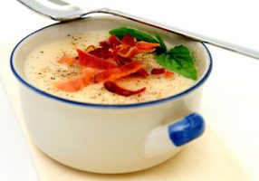Potato soup topped with crisp bacon and fresh Basil leaves served in a rustic blue and white bowl